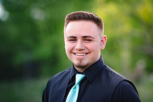 Chris Naranjo is wearing a dress shirt and tie and is smiling for the camera.