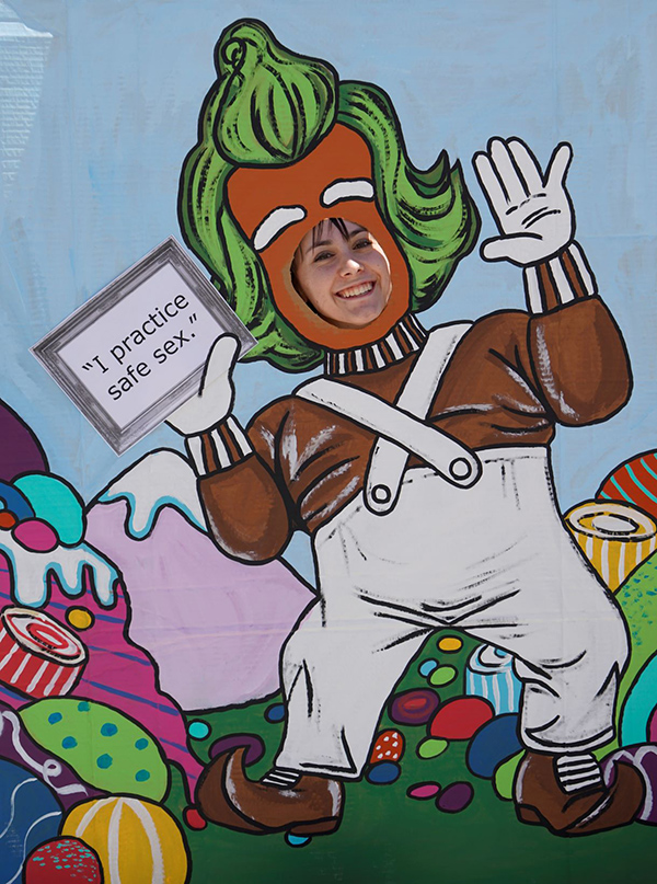 A student poses behind a "I practice safe sex" cartoon cutout poster.