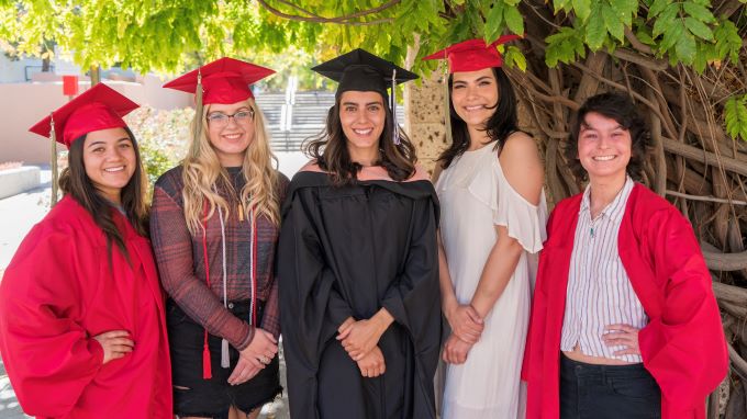 SHAC Health Promotion Graduates dressed in caps and gowns pose in front of a tree at UNM.