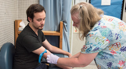 A lab tech performs a blood draw on a male student.