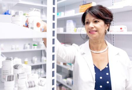 A SHAC Pharmacist reaches for a pill bottle from a shelf.