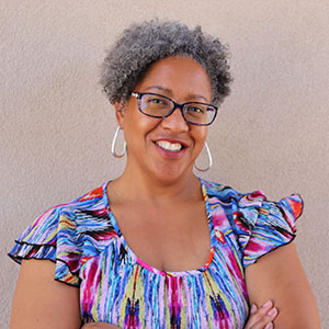 Stephanie Mciver poses in front of an adobe wall.