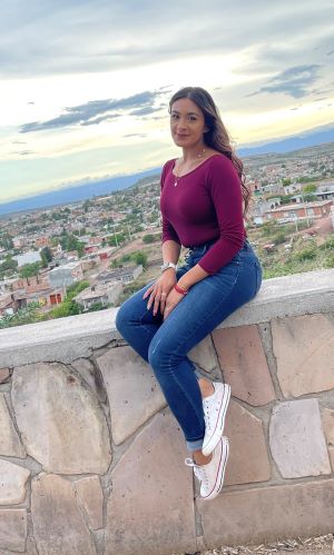 Lisbeth Duron Pacheco is sitting on a rock wall with the city of Albuquerque in the background.