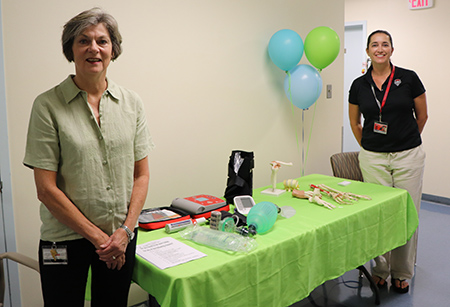 Two medical providers stand next to a table with educational materials.