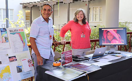 Two SHAC staff pose behind a table outside SHAC with educational materials and posters about travel health.