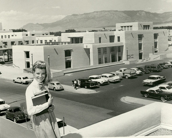 A young woman holding books poses in front of parking lot next to SHAC.